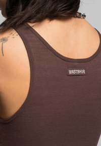 Brown tank top with a scoop neckline and narrow straps, featuring a small logo patch with the text "WRSTBHV" near the back. Soft, textured fabric.