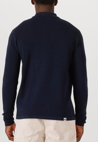 Navyblauwe geribde trui met een polo kraag en lange mouwen, met een zijlabel, van achteraf weergegeven, met een gladde textuur.