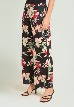 Sorte bukser med vide ben med rød, beige og grøn blomsterprint, båret med sorte hælsandaler med stropper og en sort top.