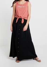 Sort maxi-nederdel med en række knapper ned foran og en løs pasform. Kombineret med en pink ærmeløs top, der er knyttet ved taljen.