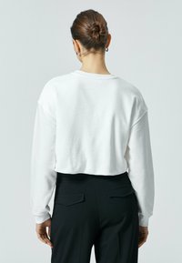 Witte cropped sweatshirt met een ronde halslijn en verlaagde schouders, gecombineerd met hoge zwarte broeken met twee achterzakken.