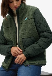 Groene gewatteerde jas met een pluizige, fuzzy bovenkant en een gladde onderkant. Ritsluiting met zijzakken en elastische manchetten.