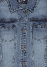 Jeansová bunda ve světle modré barvě, se zapínáním na knoflíky vpředu, dvěma náprsními kapsami a kontrastním prošitím. Látka má texturovaný povrch.