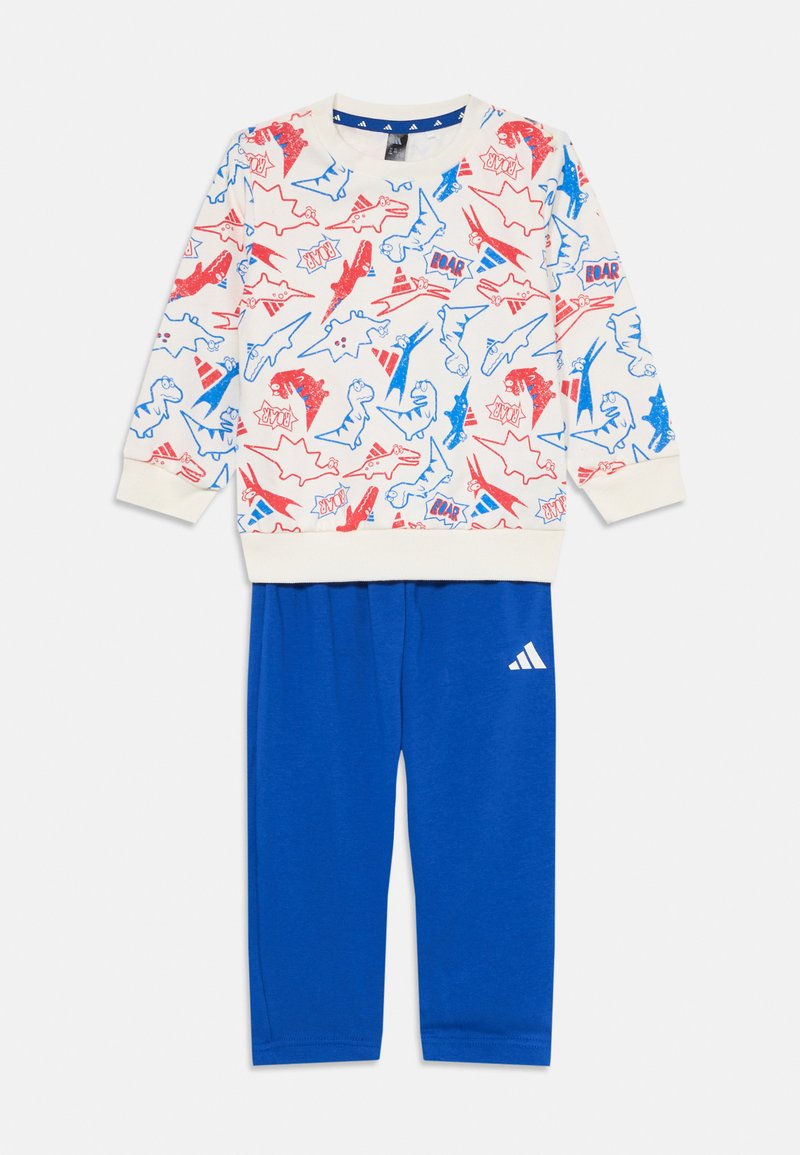 Kokvilnas džemperis ar dinozauru un supervaroņu attēliem sarkanā un zilā krāsā, apvienots ar ziliem kokvilnas biksēm, kurām ir balta Adidas logo.