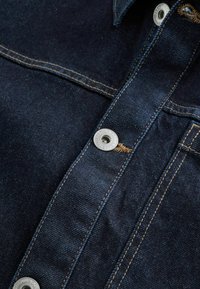 Dark denim shirt featuring silver metal buttons, contrasting golden stitching, and a classic collar design. Smooth texture with visible seams.