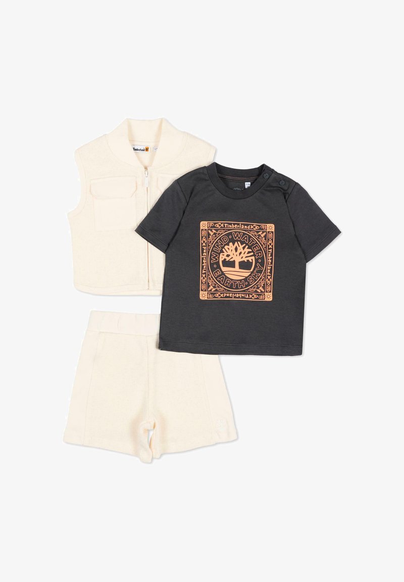 Ensemble trois pièces pour tout-petit comprenant un gilet en maille crème et un short assorti, ainsi qu'une chemise noire à manches courtes arborant un logo Timberland orange et un motif inspiré de la nature.