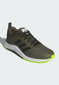 Grüner Sportschuh mit schwarzen Streifen, strukturierter Oberseite, weißer und neongrüner Sohle, mit gepolstertem Kragen und Schnürdesign.