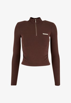 Brązowa bluzka z długim rękawem i prążkowanym wzorem, z wysokim kołnierzem, zamkiem błyskawicznym do połowy oraz srebrnym akcentem na lewej piersi. Miękka tekstura.