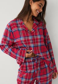 Rødt og blåt ternet pyjamasæt med en knappet bluse med lange ærmer og bukser med snøre i taljen. Blødt stof.