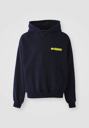 Marineblauwe hoodie met een voorzak en gele "MISBHV"-logo op de bovenste linkerborst, weergegeven op een witte achtergrond.