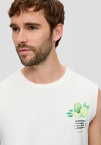 White sleeveless t-shirt made of cotton, featuring a green lime graphic with leaves and text "GUARANTEED GENUINE 100% PURE SUMMER."