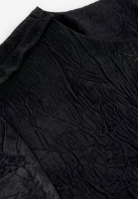 Black wrinkled fabric with a soft texture, featuring a rounded neckline and a mix of smooth and crinkled surfaces. Minimalist design.