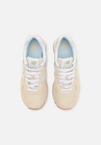 Beige sportovní boty z semišových a síťovinových materiálů, bílé tkaničky, polstrované límce a texturovaná gumová podrážka. Vlastnosti: logo na jazyku.