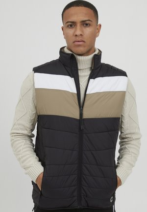 Chaleco acolchado en negro, beige y blanco. Presenta un alto cuello, cierre de cremallera y un cuello de tortuga de punto texturizado debajo. Bloques de color en contraste.