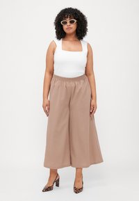 Beige wide-leg pants with an elastic waistband paired with a fitted white sleeveless top and leopard print heels. Curly hair and sunglasses.