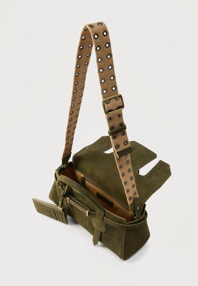 Sac à main en daim vert olive avec une large sangle beige ornée d'œillets métalliques, rabat partiellement ouvert et poche avant zippée avec petite pochette attachée.