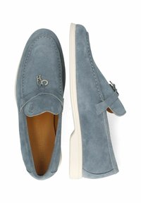 Mocassini in suede blu chiaro con suola in gomma bianca, caratterizzati da un design con cuciture e un accento metallico del logo sulla parte superiore.