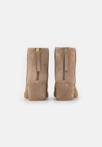 Beige mokkasukot nilkkurit, joissa on matala lohko korko ja takakiinnitysvetoketju. Teksturoitu päällinen ja sileä pohja, jossa on kultaa vetoketjun varusteet.