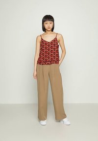 Top vermelho sem mangas com padrão e decote redondo combinado com calças largas bege. Ténis brancos completam o conjunto.