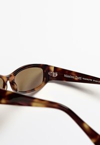 Occhiali da sole tartarugati con una finitura lucida, lenti leggermente ovali e un logo argentato sulla asta. Bordo arrotondato e liscio.