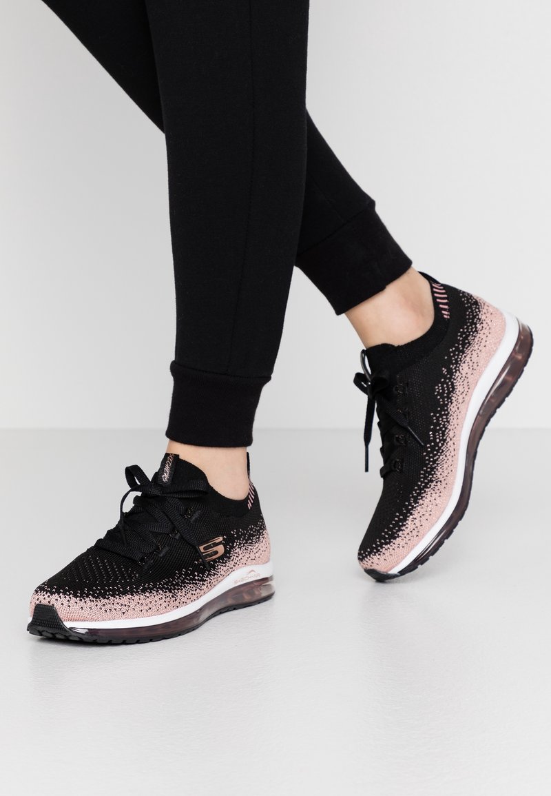 Svarta träningsskor med en gradient rosa prickad design, nätöverdela och vadderad sula. Har snörning och en logotyp på sidan.