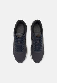 Ciemnoniebieskie sneakersy z gładką cholewką z tkaniny, wiązaniem, okrągłym noskiem i kontrastującą białą gumową podeszwą. Złoty detal logo na języku.