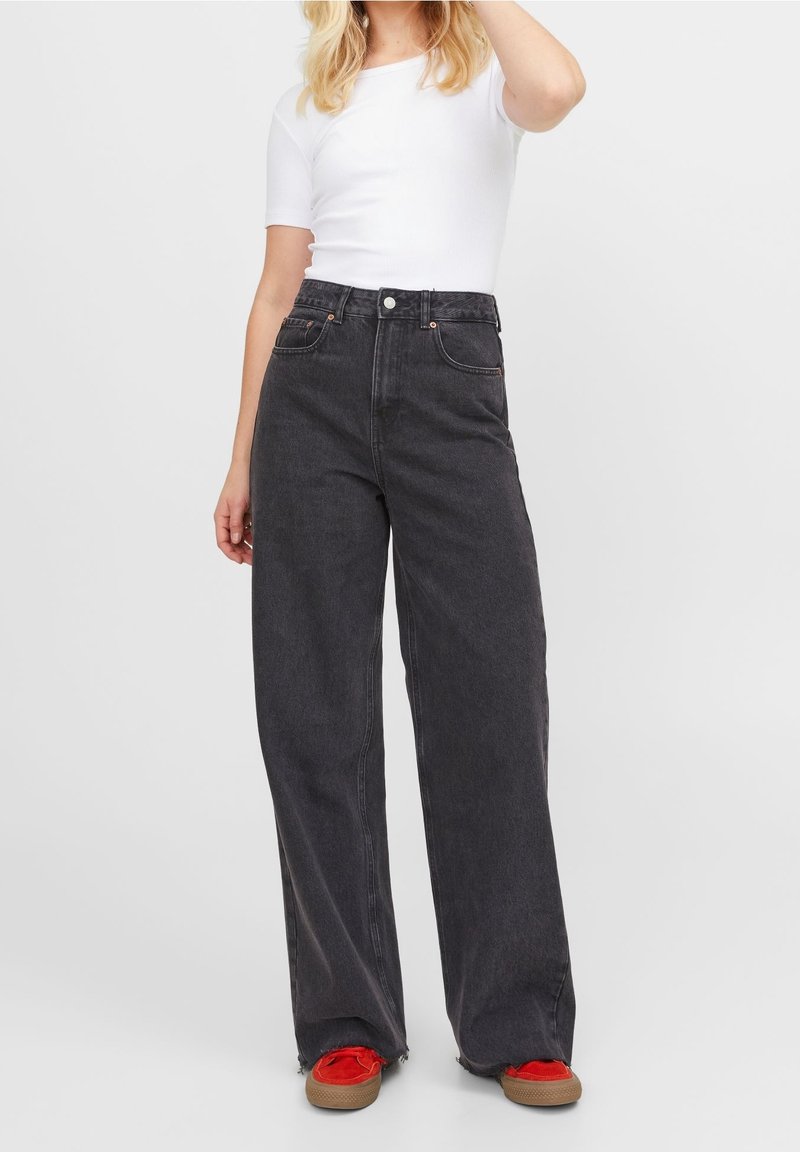 Svarta denimjeans med vida ben och hög midja, med orangea sömmar, två framfickor och knappstängning. Matchat med en vit topp.