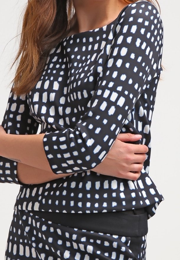 Haut à motifs noir et blanc avec un large col, des manches trois-quarts et un ourlet peplum, fabriqué à partir d'un tissu lisse et léger.
