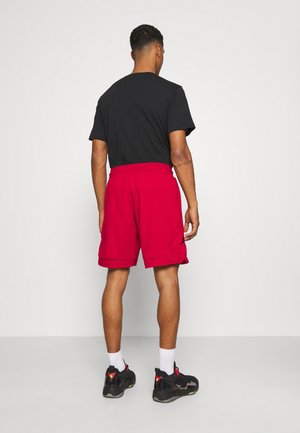Rode shorts met een ontspannen pasvorm, voorzien van een elastische tailleband en zijzakken, gecombineerd met een zwart T-shirt en zwarte sportschoenen.