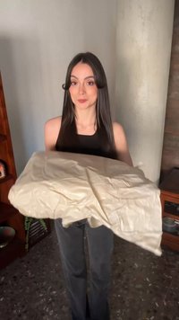 Vrouw met lang donker haar, gekleed in een zwart mouwloos shirt, houdt binnen een gekreukeld beige stuk stof of plastic vast.