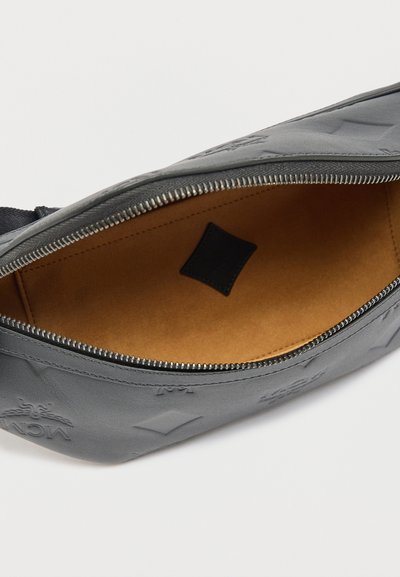 Γκρι δερμάτινη θήκη με φερμουάρ και ανάγλυφο μοτίβο λογότυπου, ανοιχτή για να αποκαλύπτει εσωτερικό από ταμπά σουέτ και μικρή μαύρη ορθογώνια ετικέτα στο εσωτερικό.