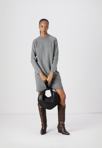 Vestido cinza de mangas longas com um corte descontraído, combinado com botas cowboy de couro castanho e uma bolsa circular preta. Textura suave e design simples.