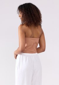 Strapless, lichtbruin top gemaakt van zachte stof, gecombineerd met witte, losse, gestructureerde broek met een elastische tailleband.