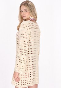 Strickkleid in Creme mit Ajourdesign, langen Ärmeln und lässiger Passform. Auffällig ist das strukturierte Muster und die legere Silhouette.
