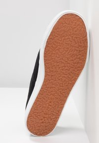 Baskets en toile noire avec une semelle orange en caoutchouc texturée et des accents blancs sur les côtés. Présente une forme plate et un design minimaliste.