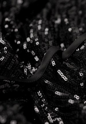 Sort stof med teksturerede pailletter i varierede størrelser, der har en glat sort bånddetalje langs kanten.