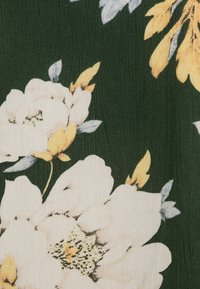 Vita och gula blommor med grå blad tryckta på mörkgrön strukturerad textil.