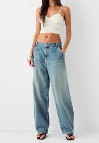 Bílý krajkový crop top s tenkými ramínky, v kombinaci s světle modrými, volnými, širokými džínami s předními kapsami a klasickým zapínáním na knoflík.