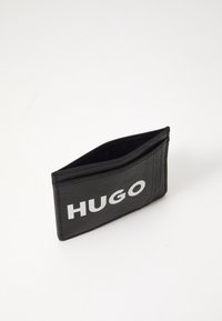 Portafoglio in pelle nera con finish testurizzato. Presenta un logo "HUGO" bianco prominente sul fronte e diverse fessure per carte.
