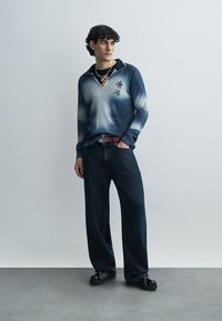 Μπλε πλεκτό πουκάμισο ομπρέ με γιακά, με κεντημένη λεπτομέρεια. Συνδυασμένο με φαρδιά σκούρα τζιν και μαύρα παπούτσια.