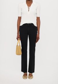 Svarta utsvängda jeans, ribbad vit kortärmad topp med snörning i halsen, vävd gul handväska och bronzfärgade flator i vävt material. Slät textur, avspänt stil.