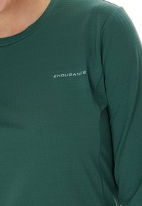 Donkergroen shirt met lange mouwen van gladde stof. Bevat een klein wit "ENDURANCE" logo op de borst. Eenvoudig, aansluitend ontwerp.