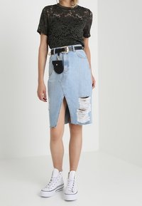 Camiseta de encaje negro, falda de mezclilla azul claro con abertura frontal y áreas desgastadas, combinada con zapatillas altas blancas y un cinturón negro.