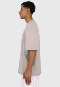 Lys grå kortærmet t-shirt lavet af bomuld, med en afslappet pasform og minimalistisk design. Sømmen er lige med lette sideslids.