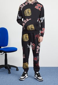 Conjunto de sudadera con capucha y pantalones deportivos negros con gráficos audaces, que incluyen anillos de campeonato dorados y el número 23, combinado con zapatillas blancas contrastantes.