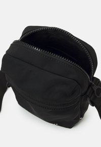Borsa a tracolla nera in nylon con chiusura a zip, caratterizzata da una texture liscia e una tracolla regolabile. L'interno include una tasca aggiuntiva con zip.