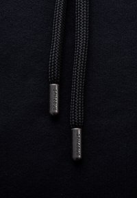 Schwarzer Hoodie aus strukturiertem Stoff, mit geflochtenen Zugbändern und metallischen Aglets, die mit "SPITZBUB" graviert sind.