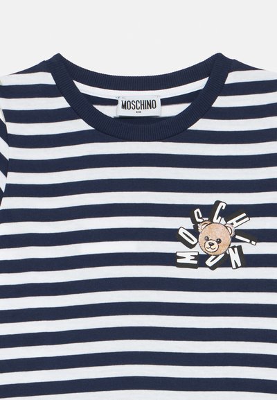 Μπλε ναυτικό και λευκό ριγέ μπλουζάκι με ριμπ ύφασμα στον γιακά. Διαθέτει γραφικό αρκούδας με το κείμενο "MOSCHINO" σε μαύρο, κεντραρισμένο στο στήθος.