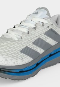 Λευκό και γκρι παπούτσι τρεξίματος Adidas Adistar με υφή στην επάνω επιφάνεια, λευκά κορδόνια και μπλε απορρόφηση κραδασμών στη γκρι σόλα.