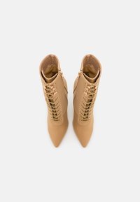 Bottes beige à la cheville avec un bout pointu, dotées d'un laçage à l'avant et de ferrures dorées. Matière lisse avec une doublure douce.